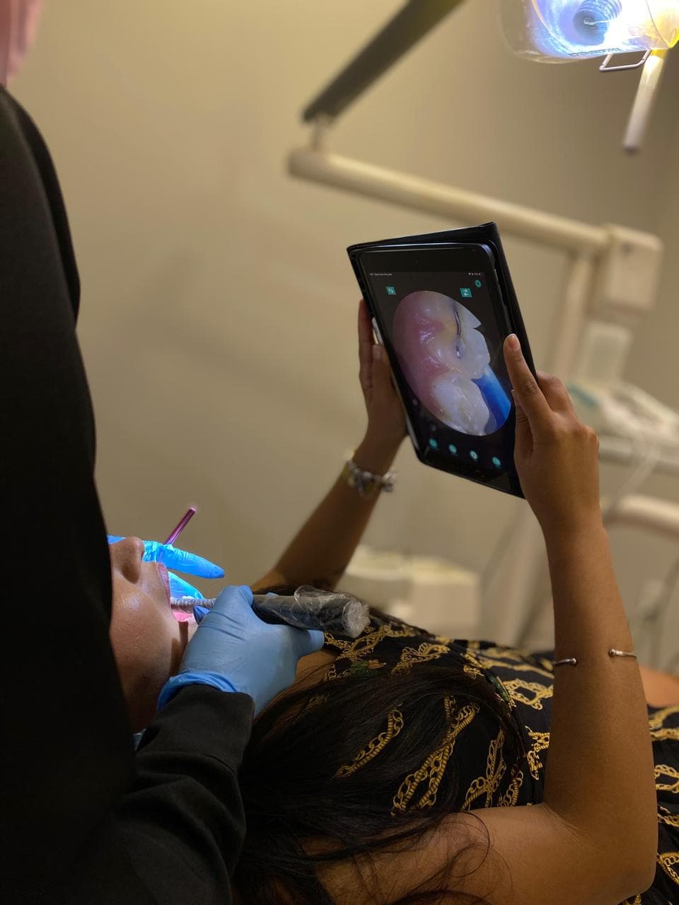 Paciente deitada na cadeira segurando um tablet que mostra, ampliado e ao vivo, o próprio dente sendo examinado